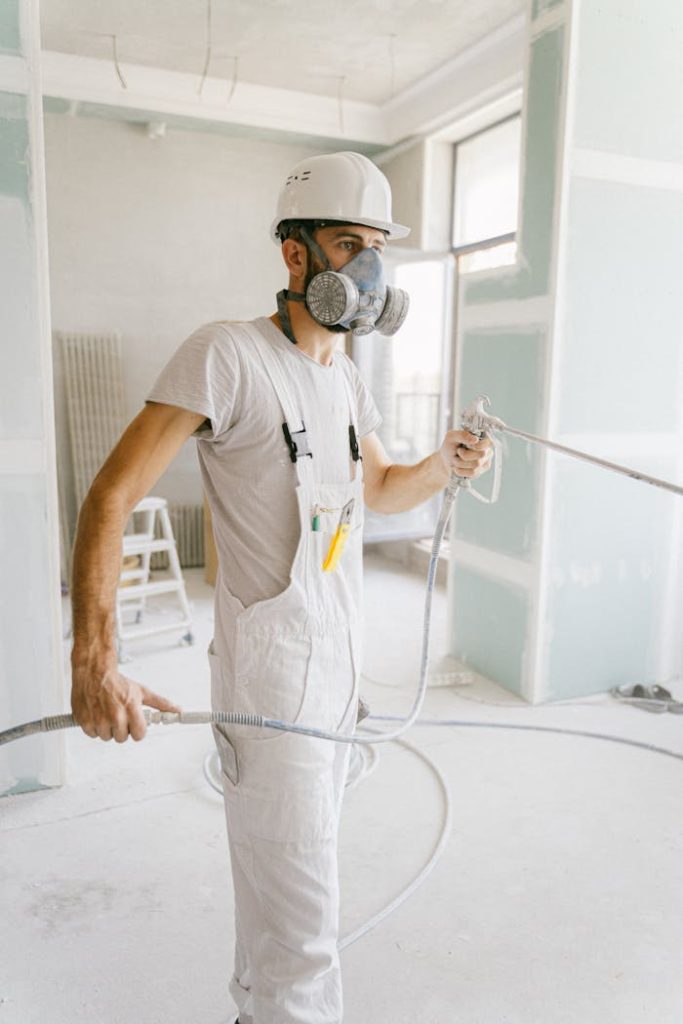 a-man-wearing-gas-mask-and-hard-hat-using-a-hose-5493660 A construction worker wearing a gas mask and holding a hose in a renovation site.