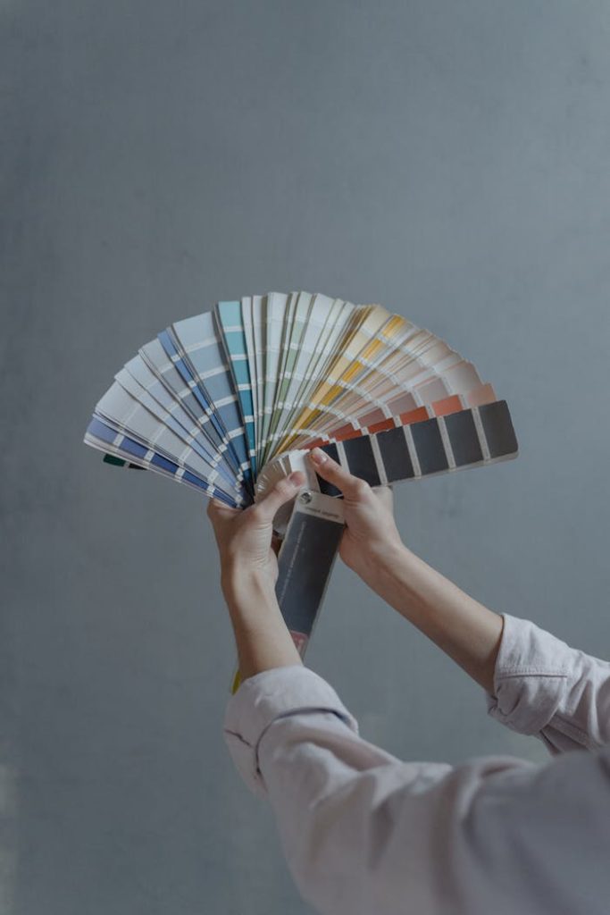 person-holding-blue-white-and-red-hand-fan-6474446 Hands displaying a fan of paint color swatches against a gray wall, ideal for home renovation projects.